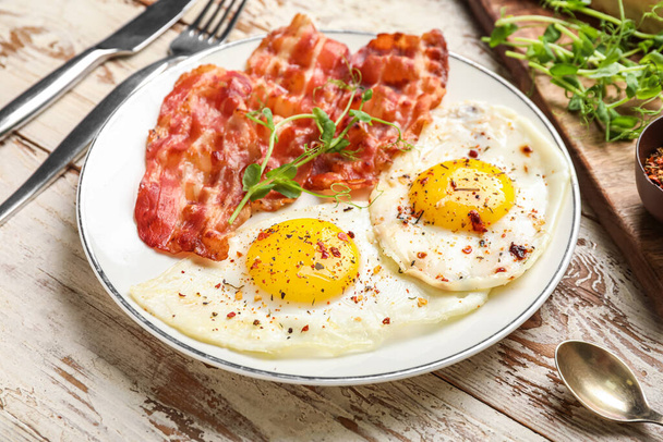 Plate with tasty fried eggs with bacon and spices on light wooden table, closeup - Φωτογραφία, εικόνα