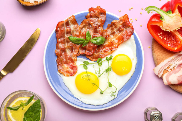 Plate of tasty fried eggs and bacon on pink background - Фото, изображение