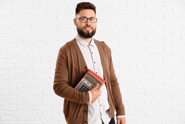 Handsome Math teacher with calculator and books on white brick background - Fotografie, Obrázek
