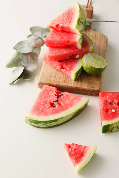 Cutting board with slices of watermelon, lime and eucalyptus branch on white background - Foto, Bild