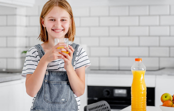 Preteen girl with orange juice bottle and glass at kitchen. Pretty child kid with vitamin fruit drink at home - Fotografie, Obrázek