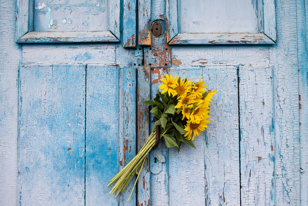 Bouquet of sunflowers on a blue wooden background. Old blue wooden door with yellow flowers. Copy space - 写真・画像