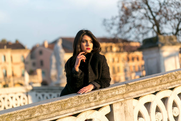 красива італійська дівчина з червоною сукнею і чорною курткою на мосту на площі Падуї. Фотографія високої якості - Фото, зображення