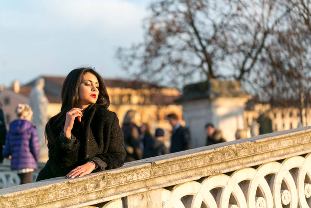 beautiful Italian girl with red dress and black jacket on the bridge in the square in Padua. High quality photo - Photo, Image