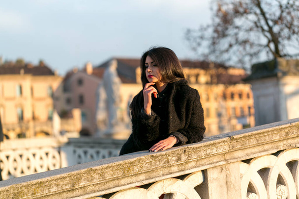 beautiful Italian girl with red dress and black jacket on the bridge in the square in Padua. High quality photo - 写真・画像