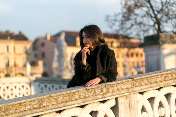 beautiful Italian girl with red dress and black jacket on the bridge in the square in Padua. High quality photo - 写真・画像