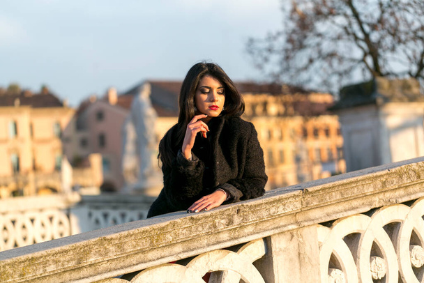 beautiful Italian girl with red dress and black jacket on the bridge in the square in Padua. High quality photo - Photo, image