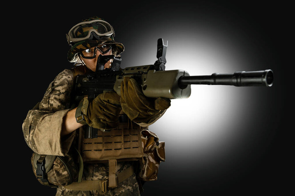Woman army soldier in combat uniforms with assault rifle, plate carrier, goggles and backpack. Studio shot, dark background - Foto, Imagen