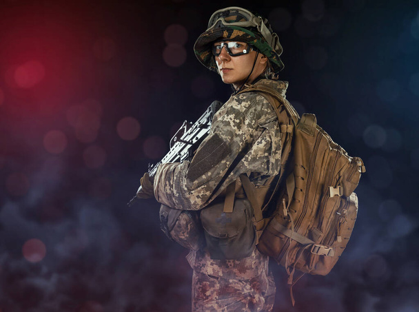 Woman army soldier in combat uniforms with assault rifle, plate carrier, goggles and backpack. Studio shot in smoke, dark background - Photo, image