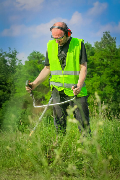 Worker mowing grass with grass trimmer - Zdjęcie, obraz