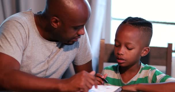 Niño haciendo la tarea en casa, padre africano ayudando a su hijo con el estudio - Metraje, vídeo