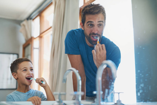 Make sure you get those teeth at the back. a handsome young man and his son brushing their teeth in the bathroom - Fotó, kép