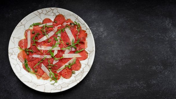 Meat carpaccio with parmesan cheese and arugula, on gray concrete - Fotografie, Obrázek