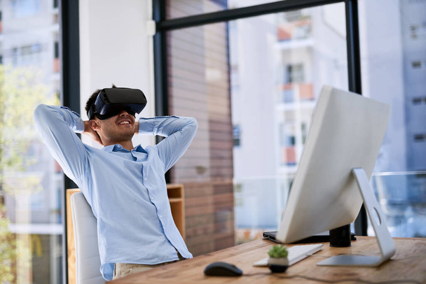 Another job well done with the help of technology. a happy young businessman wearing a virtual reality headset while working at his desk in the office - Фото, зображення