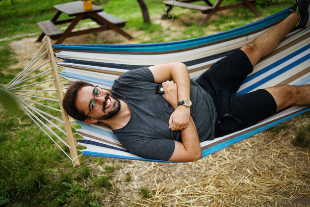 young happy caucasian man swinging in a hammock on a pleasant summer weekend morning in garden.  - Foto, Imagen