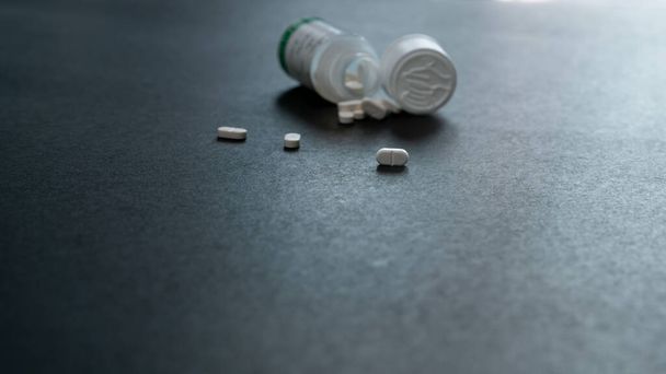 White tablets pills and blur plastic pill bottle on dark floor. Prescription drugs. Pharmaceutical industry. Medical care. Medication for cure illness. Pharmacy. Small white pills. Dose recommended. - Photo, Image