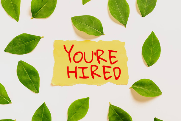Sign displaying You Re Are Hired, Word for New Job Employed Newbie Enlisted Accepted Recruited Blank Paper Surrounded With Leaves For Wedding Invitation And Cards. - Foto, Imagem