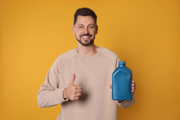 Man holding blue container of motor oil and showing thumbs up on orange background - Foto, Imagem