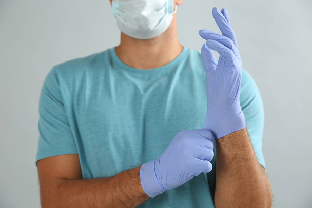 Man in protective face mask putting on medical gloves against grey background, closeup - Foto, Imagen