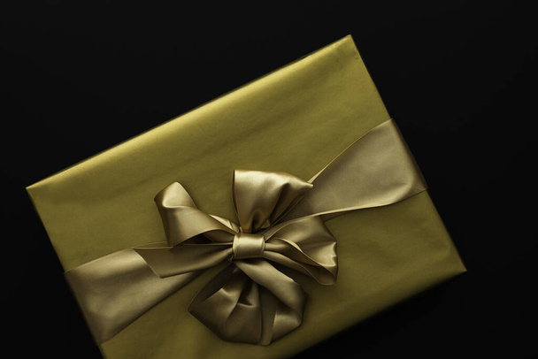 Confezione regalo in involucro dorato con fiocco primo piano su fondo nero - Foto, immagini
