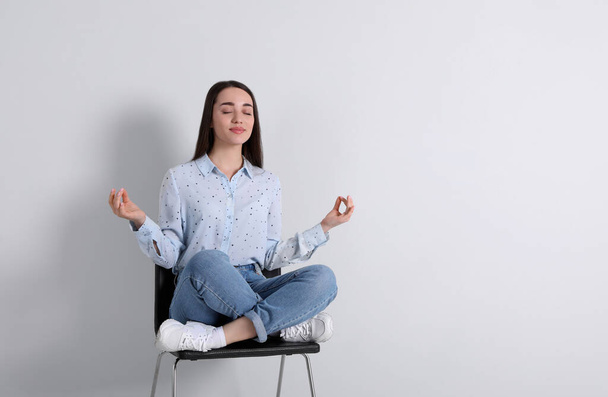 Young woman meditating on chair near white wall in office, space for text - Foto, Imagem