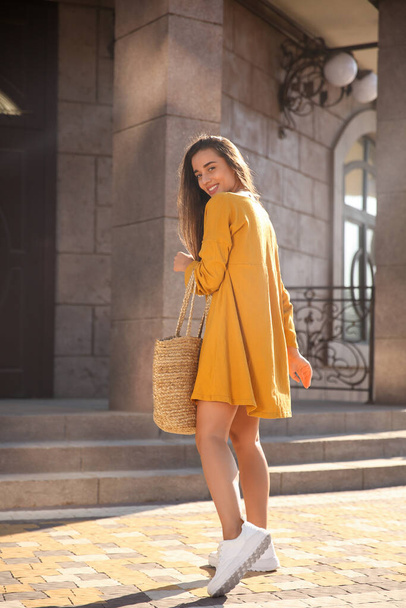 Beautiful young woman in stylish yellow dress with handbag on city street - Fotoğraf, Görsel