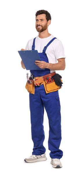 Professional plumber with clipboard and tool belt on white background - Foto, imagen