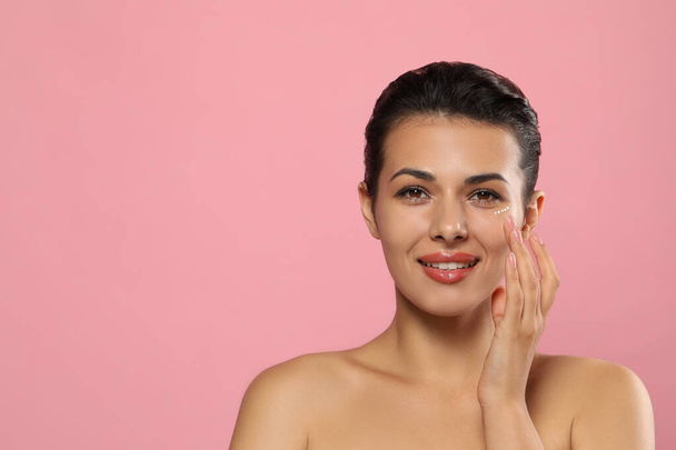 Woman applying cream under eyes on pink background, space for text. Skin care - Zdjęcie, obraz