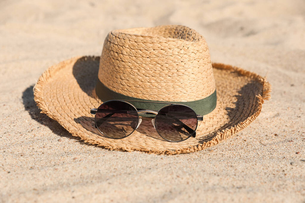 Stylish straw hat and sunglasses on sandy beach - Fotó, kép