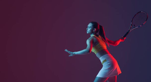 Young woman, professional tennis player training isolated on blue background in neon. Healthy lifestyle. The practicing, fitness, sport, exercise concept. The female model in motion or movement - Φωτογραφία, εικόνα