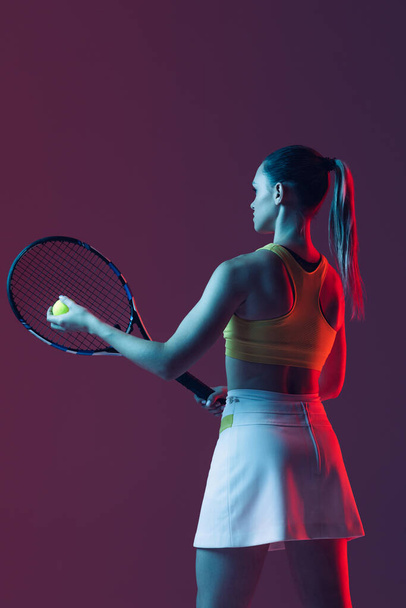 Champion. Young woman, professional tennis player training isolated on blue background in neon. Healthy lifestyle. The practicing, fitness, sport concept. The female model in motion or movement - Photo, Image