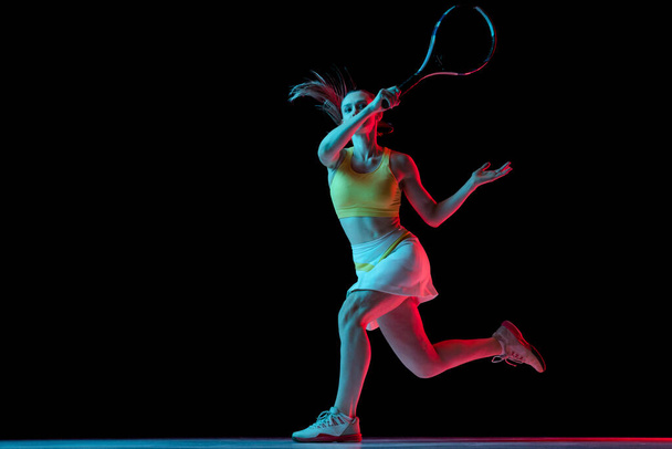 Young woman, professional tennis player training isolated on blue background in neon. Healthy lifestyle. The practicing, fitness, sport, exercise concept. The female model in motion or movement - Photo, image