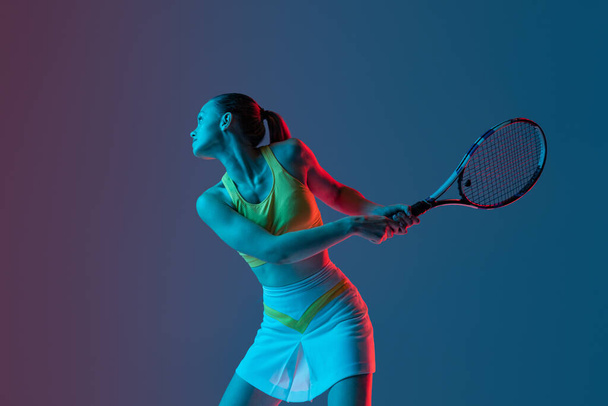 Champion. Young woman, professional tennis player training isolated on blue background in neon. Healthy lifestyle. The practicing, fitness, sport concept. The female model in motion or movement - Photo, image