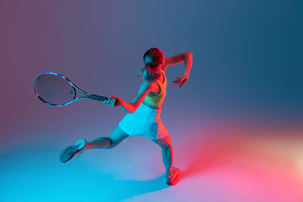Aerial view. Training of female tennis player practicing power serving isolated on dark background in neon. Sports emotions, healthy lifestyle, fitness, sport, achievements concept. - Фото, изображение