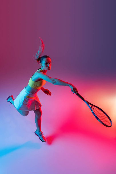 Aerial view. Training of female tennis player practicing power serving isolated on dark background in neon. Sports emotions, healthy lifestyle, fitness, sport, achievements concept. - Фото, зображення