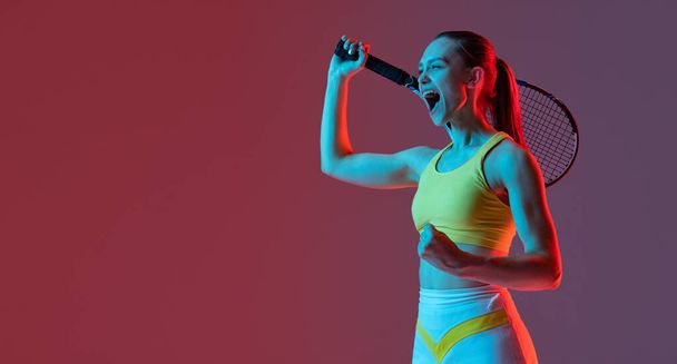 Winner emotions. Excited young woman, tennis player shouting after sports win isolated on purple background in neon. Healthy lifestyle, fitness, sport, exercise concept. - Photo, image
