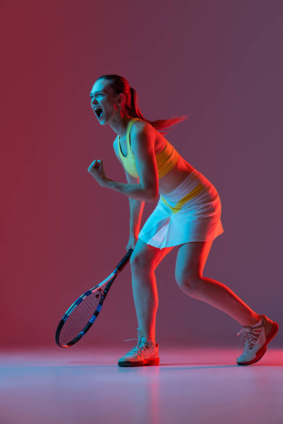 Winner emotions. Excited young woman, tennis player shouting after sports win isolated on purple background in neon. Healthy lifestyle, fitness, sport, exercise concept. - Fotoğraf, Görsel