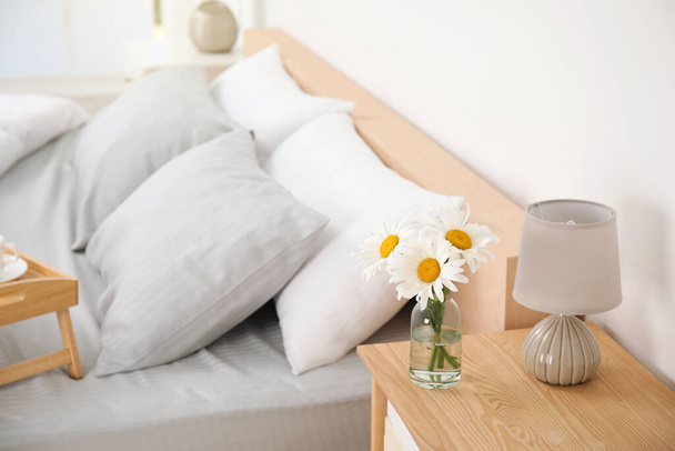 Bouquet of beautiful daisy flowers and lamp on nightstand in bedroom, space for text - Photo, Image