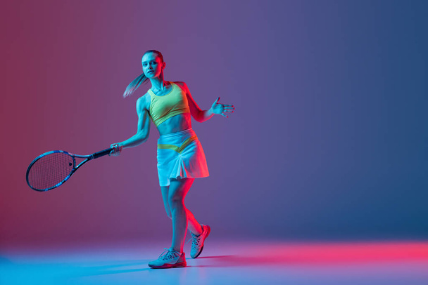 Full length portrait of young woman playing tennis isolated on dark background in neon. Healthy lifestyle. The practicing, fitness, sport, exercise concept. The female model in motion or movement - Foto, imagen