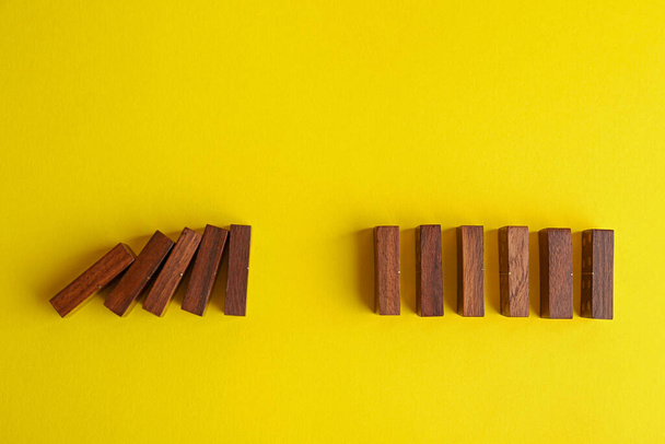 Falling and standing wooden domino tiles on yellow background, flat lay. Space for text - Foto, Imagen