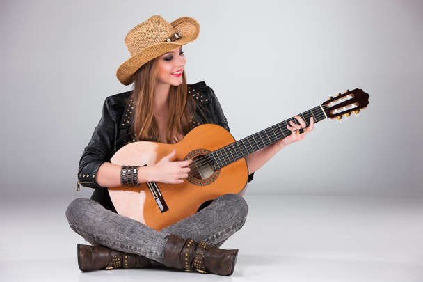 The beautiful girl in a cowboys hat and acoustic guitar. - Foto, afbeelding