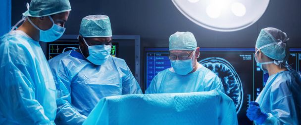 Diverse team of professional medical surgeons perform surgery in the operating room using high-tech equipment. Doctors work to save a patient in a modern hospital. The concept of medicine, technology - Photo, image