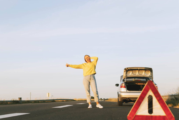 in the foreground, a red-white emergency stop sign, in the background, a girl stands with her hand raised, stops the car for help on the road, upset. Car breakdown on the road. High quality photo - Fotó, kép