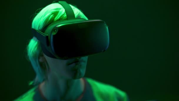 Focused man watching VR headset in neon light closeup. Blonde gamer looking goggles playing videogame over dark multi coloured background. Guy enjoying 3d movie. Future, gadgets, technology concept  - Felvétel, videó