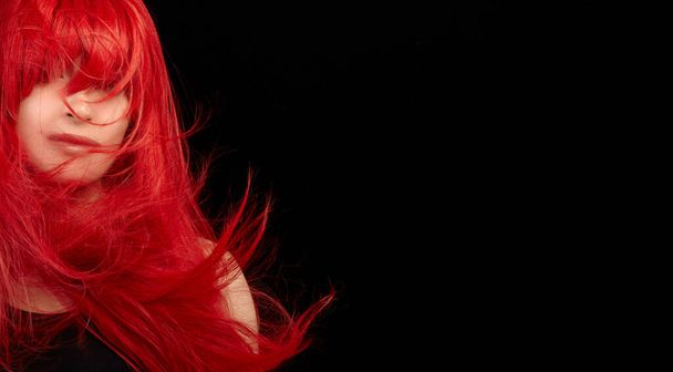 Βαμμένα μαλλιά φροντίδα και μόδα έννοια. Μόδα μοντέλο κορίτσι με ανεμοδαρμένα μακριά βαμμένα κόκκινα μαλλιά. Όμορφη κοκκινομάλλα με λαμπερά μακριά μαλλιά. Απομονωμένα σε μαύρο με αντιγραφικό χώρο - Φωτογραφία, εικόνα