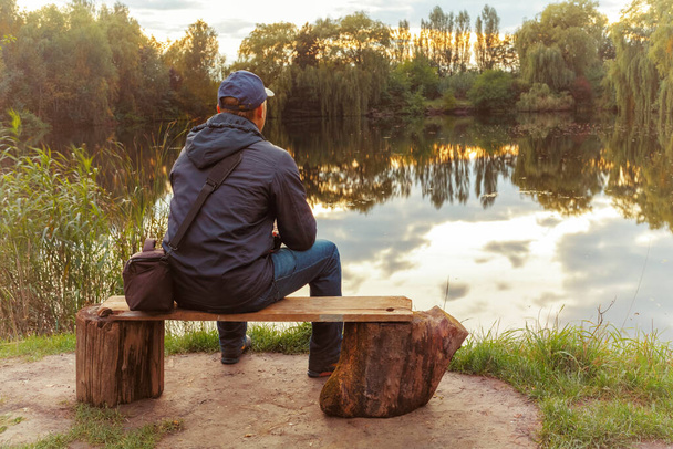 Самотній чоловік сидить на лавці біля озера. Самотній чоловік подумав
. - Фото, зображення