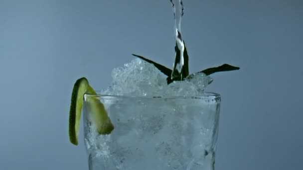 Вода наливает холодный коктейль в стекло крупным планом. Летний освежающий классический напиток. Безалкогольный напиток с мятным ломтиком лайма. Изготовление газированного мохито-лимонада для празднования выходных. - Кадры, видео