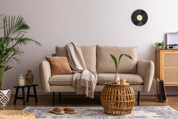 The stylish composition of living room interior with beige sofa with carpet, pillow, plaid, coffee table and personal accessories. Beige wall. Home decor. Template.  - 写真・画像