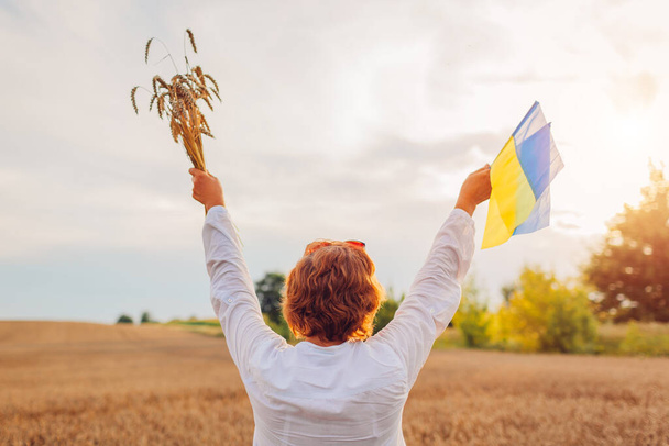 Independence Day of Ukraine. Ukrainian flag day. Happy woman raised arms with blue and yellow flags in field with bunch of wheat at sunset. Symbol of freedom. - Foto, immagini