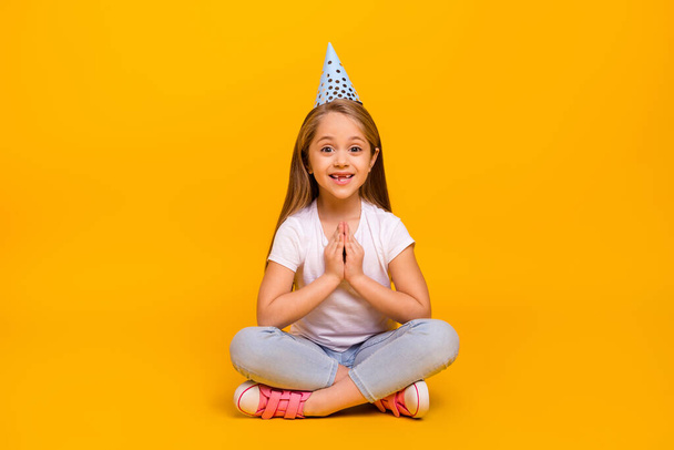Full length photo of charming excited school girl wear white t-shirt birthday cap sitting floor isolated yellow color background. - Fotografie, Obrázek